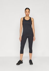 Μαύρο αθλητικό τοπ και κάπρι κολάν από ελαστικό ύφασμα, με αδιάκοπο σχέδιο και εφαρμοστή σιλουέτα. Μαύρα αθλητικά παπούτσια ολοκληρώνουν την εμφάνιση.