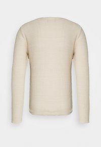 Haut beige clair à manches longues avec un motif en tricot texturé, doté d'un col rond et d'un ourlet droit, conçu pour une coupe décontractée.
