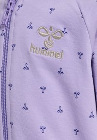 Ljuslila zip-up hoodie med små blå biepatterner och en silverfärgad "hummel"-logotyp på vänster sida av bröstet. Mjuk tygkvalitet.