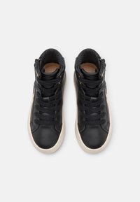 Mustat nahkaiset korkeavartiset tennarit, joissa on litteät nauhat, vaalean väriset kumipohjat ja kuvioitu sisävuori. Vetoketju sivussa.