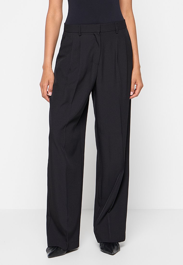 Pantaloni neri a gamba larga con vita alta, design plissettato e tessuto morbido, dotati di passanti per cintura e tasche laterali.