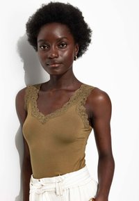 Débardeur vert olive avec dentelle au niveau du col et des épaules, en matériau doux, accompagné d'un pantalon blanc taille haute.