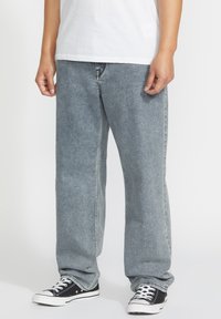 Jean en denim gris avec une coupe relaxe, des jambes droites et un léger délavage ; portés avec des baskets basses noires avec des accents blancs.