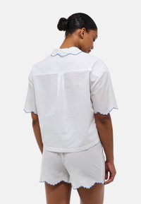 Chemise blanche en lin à manches courtes avec un col bleu en forme de vagues, assortie à un short présentant des bords découpés.