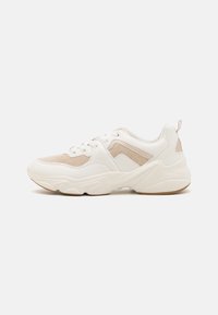 Bílé tenisky s texturovaným béžovým síťovaným svrškem, kulatou špičkou, polstrovaným límcem a gumovou podrážkou s kontrastními akcenty.