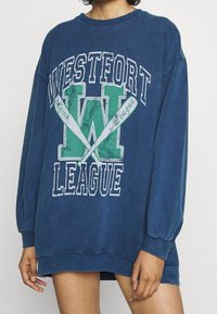 Överdimensionerad blå sweatshirt i bomullsblandning, med vit och grön trycktext "WESTFORT LEAGUE", grafisk design med roddårar och ribbade muddar.