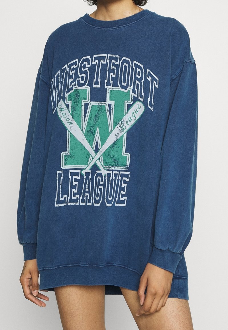 Överdimensionerad blå sweatshirt i bomullsblandning, med vit och grön trycktext "WESTFORT LEAGUE", grafisk design med roddårar och ribbade muddar.