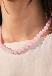 Pink beaded necklace made of smooth, round stones. Each bead is uniform in size, resting on a light-colored fabric. Subtle shine observed.