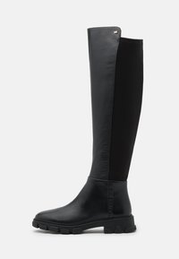 Botte noire jusqu'au genou avec un devant en cuir, un dos en tissu extensible, une semelle épaisse et un petit logo métallisé "MK" près du bord supérieur.