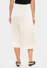Ljust beige satin midi-kjol med elastisk midja, slät textur och sidokanter för enkel rörelse. Bärs med svarta sandaler.