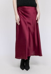 Jupe midi en satin bordeaux avec une texture lisse, un design fluide et un léger éclat, associée à des bottes à talons hauts noires et ajustées.