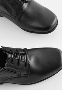 Czarne skórzane buty o gładkim wykończeniu, zaokrąglonym nosku i materiałowych sznurowadłach. Posiadają przeszywane akcenty oraz niską gumową podeszwę.