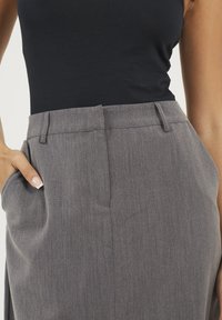 Pantaloni grigi su misura con un tessuto testurizzato, dotati di tasche laterali e frontale piatto. La vita ha passanti per la cintura e dettagli di pieghe sottili.