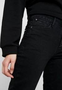 Svarta denimjeans med slim fit, subtil textur och klassisk femfickdesign. Accenteras med metallhardware och logotyp på baksidan.