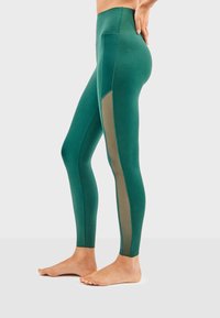 Leggings taille haute en vert foncé avec un panneau latéral contrastant beige, fabriqués en tissu extensible, conçus pour le confort et le mouvement.