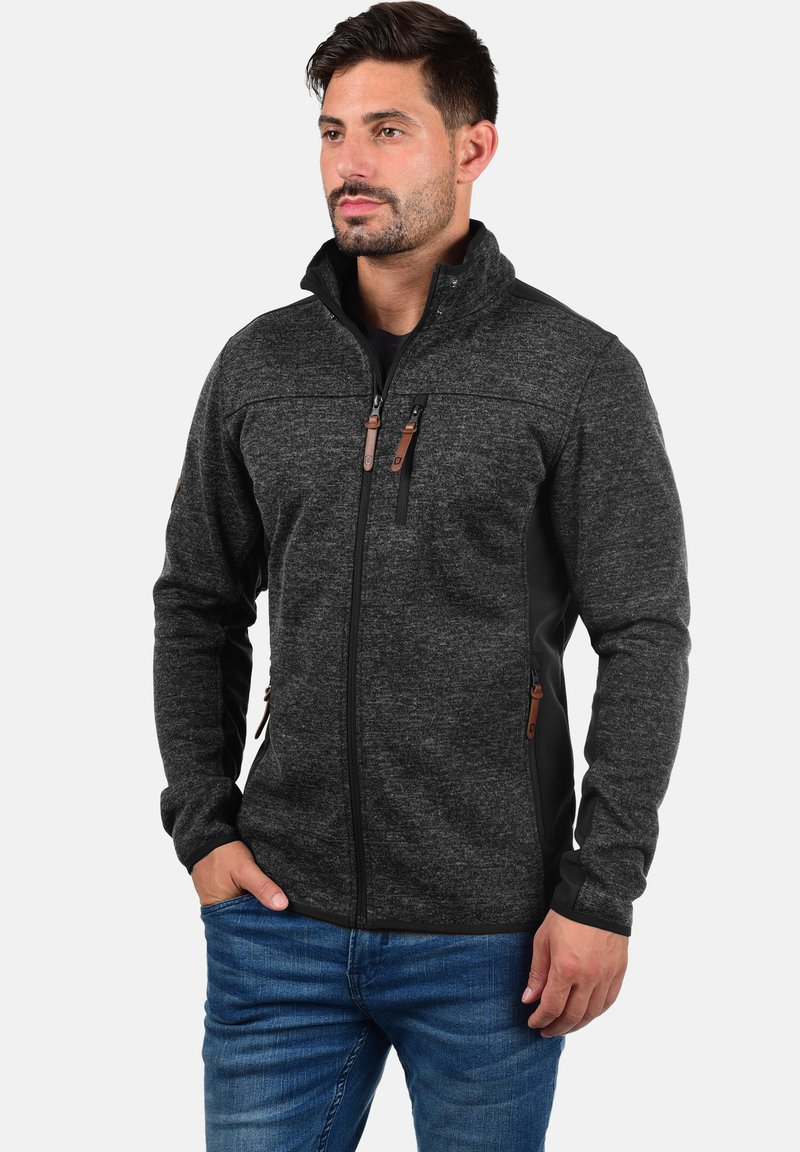 Dark gray fleece jacket with black side panels, zippered pockets, and brown accents. Features a high collar and slim fit design.