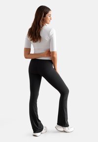 En tettsittende hvit kortermet topp kombinert med svarte vide bukser. Antrekket har en glatt tekstur og minimalistisk design.