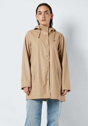 Veste imperméable beige avec capuche, fermeture à boutons-pression et poches latérales. Elle présente une texture lisse et légèrement brillante et une coupe ample.