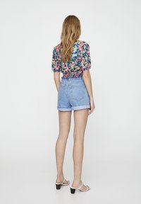 Haut de crop fleuri coloré avec des manches bouffantes, associé à un short en denim clair avec un ourlet retroussé et des sandales blanches à lanières avec un petit talon.