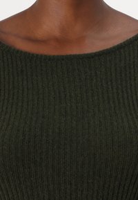 Pull en tricot vert foncé avec une texture côtelée et un décolleté large et ouvert. Le tissu semble doux et léger.