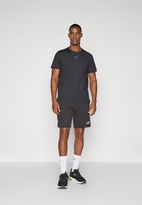 Svart treningstrøye med rund hals og Puma-logo, kombinert med svarte shorts med Puma-merke. Inkluderer hvite sokker og svarte joggesko.
