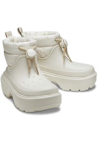 Botas blancas hasta el tobillo hechas de un material brillante con un cuello acolchado, ojetes decorativos, suela texturizada y puntos elevados para un mejor agarre.