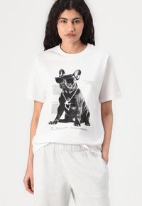 White T-shirt featuring a black-and-white graphic of a French bulldog wearing sunglasses and a chain necklace, with text beneath.