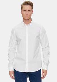 Camicia bianca a maniche lunghe con colletto classico e discreto logo sul petto, realizzata in un morbido tessuto di cotone.