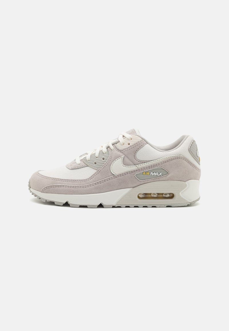 Nike Air Max 90 sneakers in light gray and white. Features suede and mesh materials, rounded shape, lace-up design, and visible air unit.