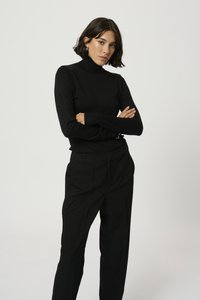 Pull en col roulé noir en tissu tricoté lisse, associé à un pantalon noir ajusté. Design simple avec des manches longues et une silhouette ajustée.