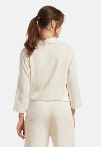 Lichtbeige, gestreepte stofoutfit met een kraag en driekwartmouwen, met een ontspannen pasvorm. De textuur lijkt glad en lichtgewicht.