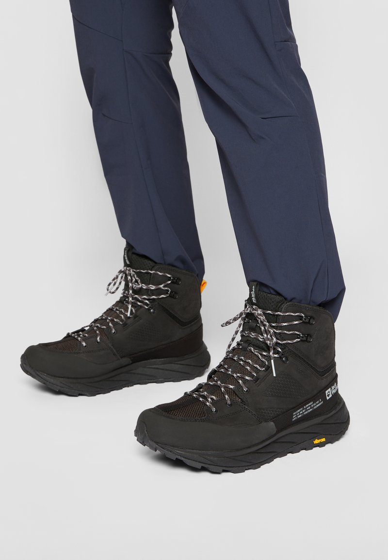 Schwarze Wanderschuhe mit einer strukturierten Oberseite, silbernen und schwarzen Schnürsenkeln sowie einem gelben Akzent. Robuste Sohle, die für den Einsatz im Freien optimiert ist.