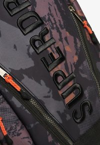 Mochila en tela de camuflaje negro y púrpura con logo en relieve, que presenta un tirador de cremallera naranja y un acabado texturizado en la superficie.