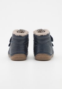 Tmavě modré kožené kotníkové boty s měkkou béžovou kožešinovou podšívkou, vybavené suchými zipy a béžovou gumovou podrážkou, s prošívaným detailem podél okrajů.