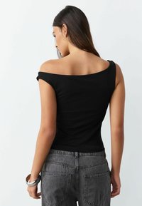 Čierny top s odhalenými ramenami vyrobený z ľahkej látky, priliehavý strih s hladkou textúrou. Kombinovaný so sivými rifľami s vreckami na zadnej strane.
