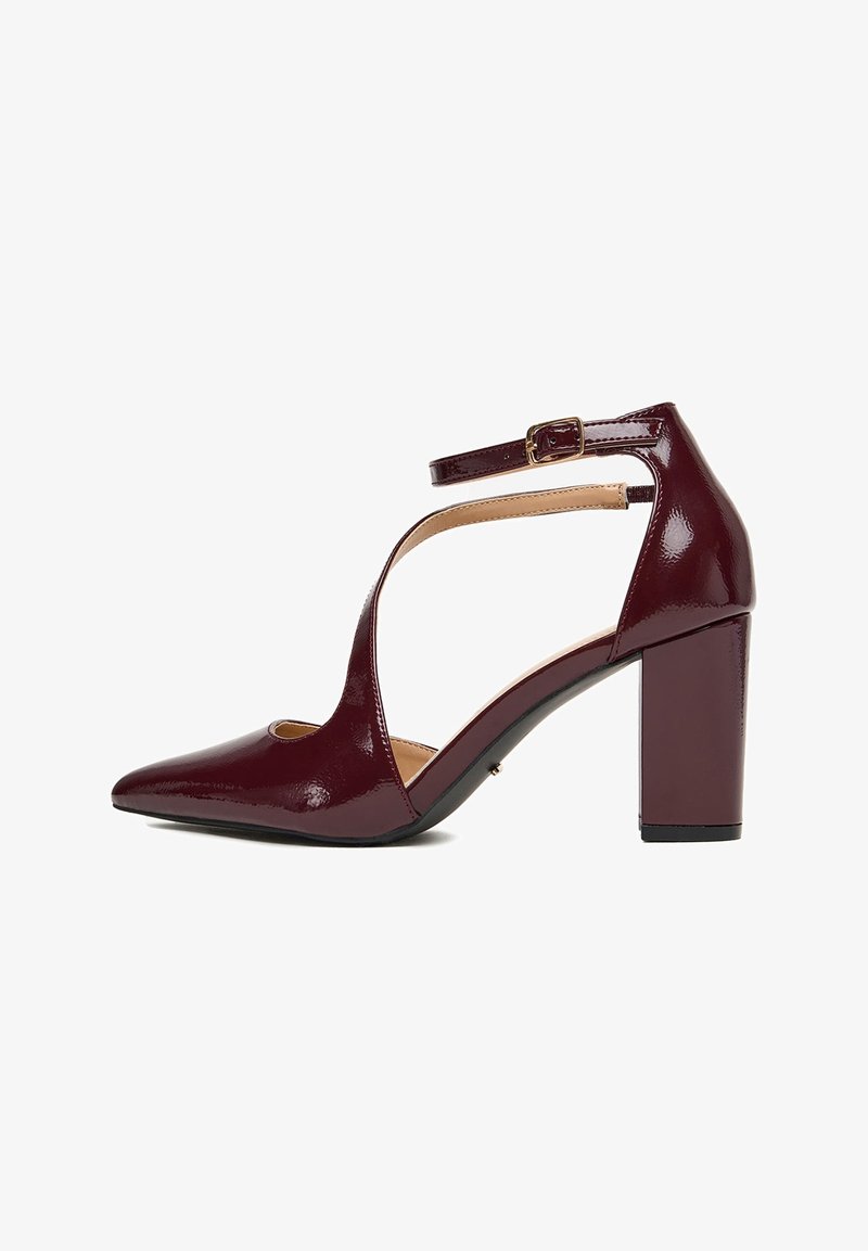 Chaussure à talon haut bordeaux brillant avec bout pointu, bride cheville, côtés découpés et talon bloc sur fond blanc.