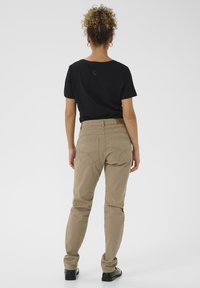 Chemise noire à manches courtes et pantalon beige avec une taille ajustée et des poches arrière. Texture de tissu lisse, design minimaliste.