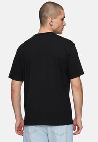 Camiseta de algodón negra con mangas cortas y diseño de cuello redondo, mostrada desde la parte de atrás sobre un fondo liso.