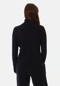 Maglione blu navy a coste con colletto alto, dotato di maniche lunghe e dettagli testurizzati lungo le braccia e sul retro. Tessuto a maglia morbido.