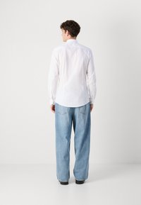 Camisa blanca de manga larga con cuello abotonado, combinada con jeans de pierna ancha de color azul claro. La camisa tiene una textura suave y un diseño ajustado.