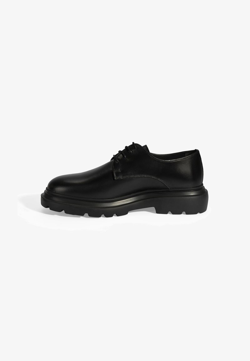 Schwarze Leder-Schuh mit glatter Oberfläche, runder Zehenpartie und dickem Gummisohle. Verfügt über Schnürsenkel und minimale Nähdetails.