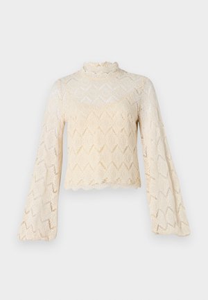 Kreemjas erilisest pitsist topp, millel on kellukesed varrukad ja kõrge kaelus. Diamantmuster üle kogu toote ja laineline äär. Läbipaistev tekstuur.