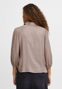 Hellbraune Bluse mit glatter Textur, dreiviertellangen Puffärmeln und abgerundetem Saum. Verfügt über einen klassischen Kragen und einen subtilen Glanz.