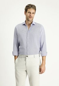 Camicia azzurro chiaro a fantasia con maniche lunghe, davanti con bottoni e polsini arrotolati, abbinata a pantaloni beige chiaro. Design su misura con una texture delicata.