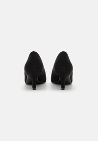Scarpe con tacco alto in suede nero, con punta affusolata, caratterizzate da una superficie liscia e tacco sottile e leggermente curvo.
