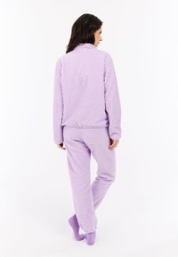Fialové flísové domáce oblečenie s textúrovaným vzorom. Vrchná časť má golier, dlhé rukávy a nohavice majú elastické manžety.