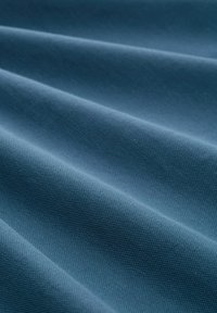 Primer plano de una tela azul texturizada con pliegues diagonales que crean suaves sombras y destellos.