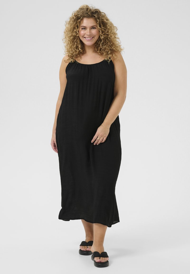 Vestido maxi negro con tirantes finos, tejido ligero, corte relajado y leve fruncido en el escote. Se lleva con sandalias negras planas.