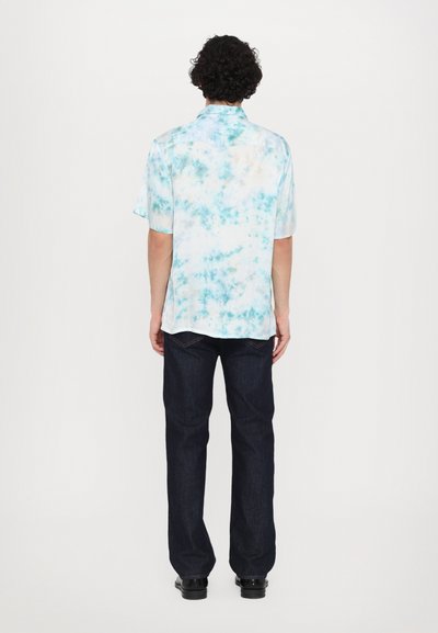 Kortærmet tie-dye skjorte i lys blå og hvid med subtile turkise accenter. Båret med mørke jeans, set bagfra.