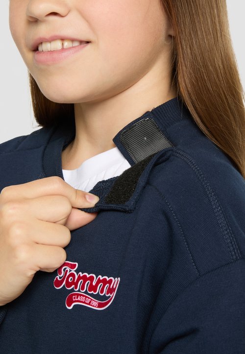 Granatowy sweatshirt z zapięciem na rzep przy kołnierzu, z czerwonym haftowanym logo "Tommy". Gładka tekstura, casualowy design.